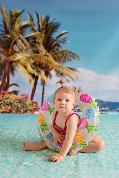 ребенок плавает в спасательном круге с арбузом возле песчаного пляжа с пальмами на берегу моря