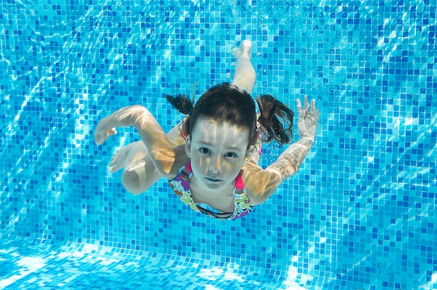 Child swims in pool underwater, happy active girl dives and has fun in water, kid fitness and sport on family vacation