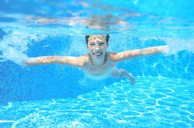 Child swims in pool underwater, happy active girl has fun under water, kid sport on family vacation