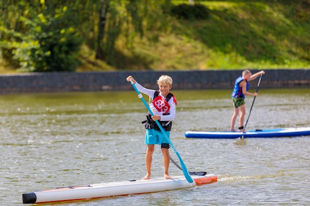 A child swims on a surfboard pushing off with a paddle Paddleboarding