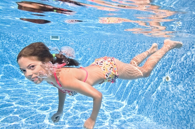 Child swims underwater in swimming pool, active girl dives and has fun under water, kid fitness and sport on family vacation