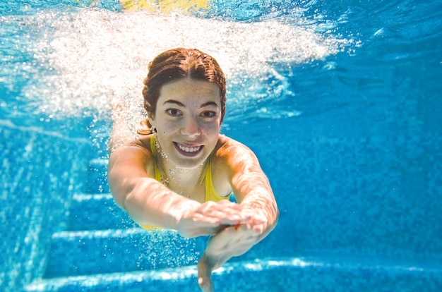 Child swims underwater in swimming pool happy active teenager girl dives and has fun under water