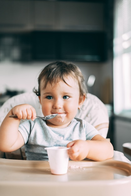 A child in a t-shirt in  kitchen eating an omelet with sausage and tomatoes with a fork