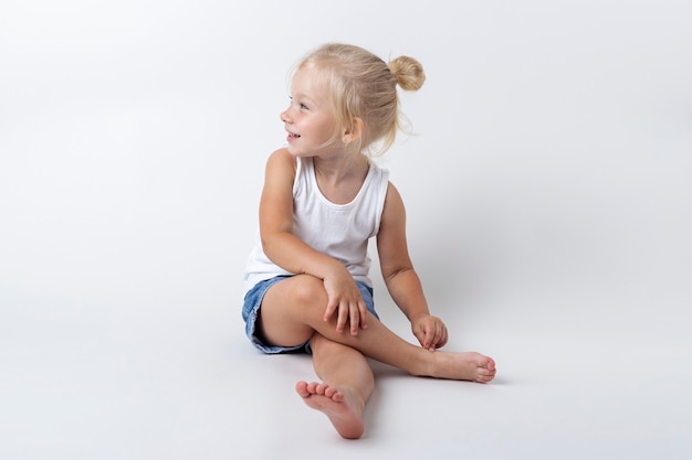 Photo child in a t-shirt, shorts sitting in the studio on a light background.