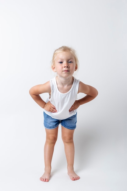 Ребенок в футболке, шортах, стоя в студии на светлом фоне.