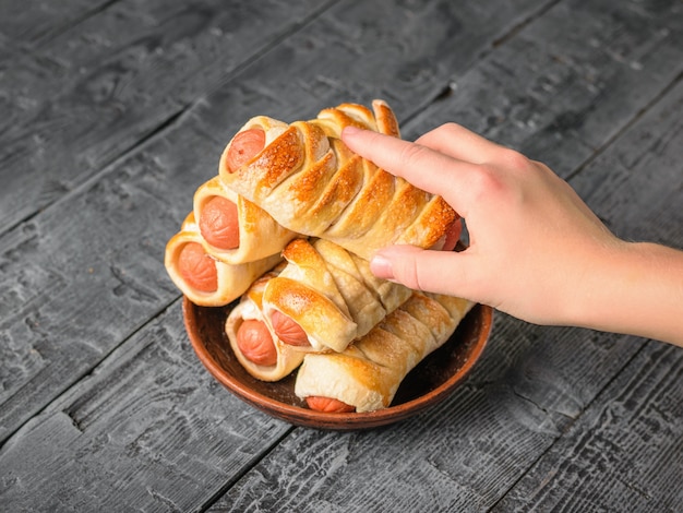 The child takes his right hand sausage dough from a clay bowl. Tasty meat snack made of dough and sausages.