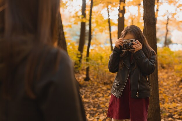 Bambino che scatta una foto a sua madre con una fotocamera retrò negli hobby del parco autunnale e nel concetto di svago