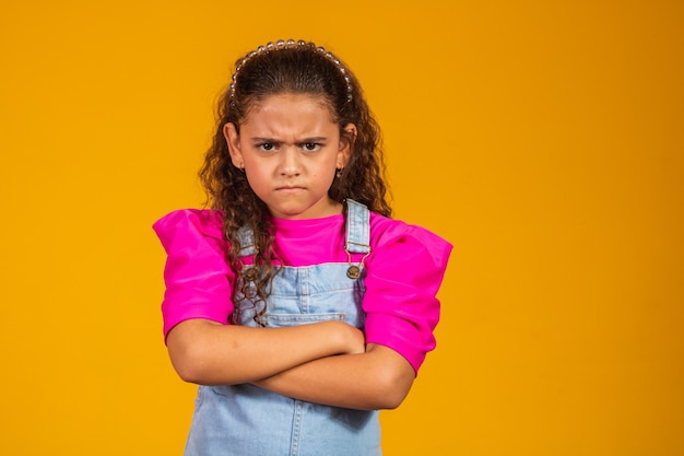 Photo child tantruming crossing the arms. on yellow background.