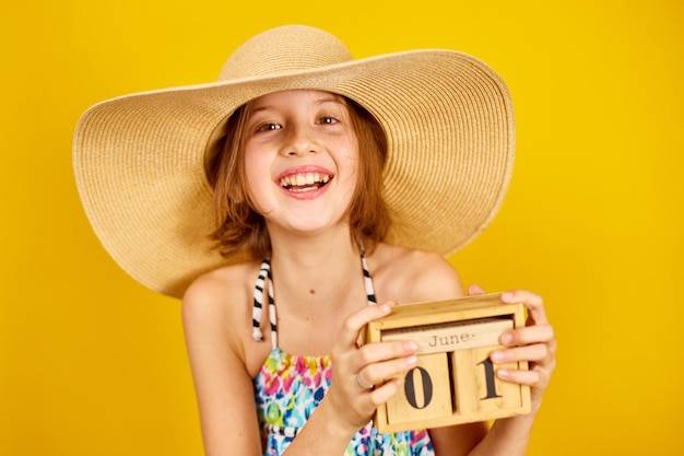 Child teenager girl in swimsuit and straw hat hold in hand wooden calendar