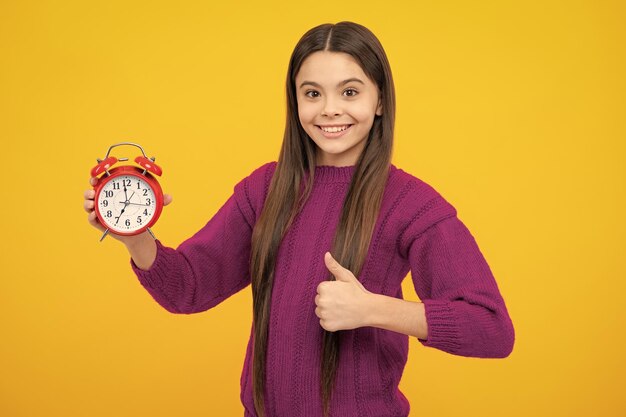 Child teenager girl with alrm clock isolated on yellow background time and deadline concept
