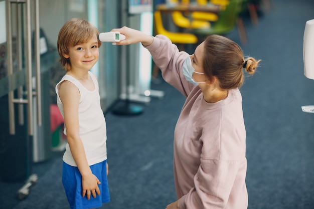 Child temperature measurement woman by laser thermometer at kindergarten