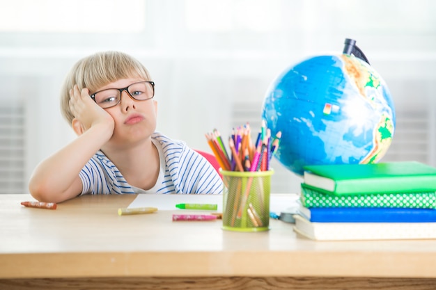 子供は学ぶのに疲れました。不幸な学生。小さな男の子を使い果たした。教室の少年。宿題を作る子供。