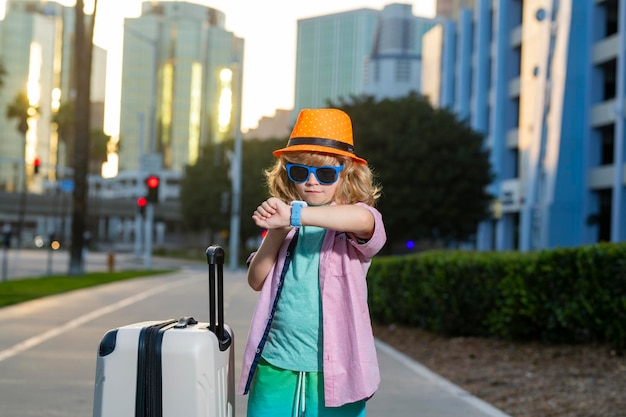 Foto bambino turista con borsa da viaggio in viaggio bambino con valigia a passeggio per la strada della città all'aperto viaggiatore bambino turista in abiti casuali e cappello porta valigia