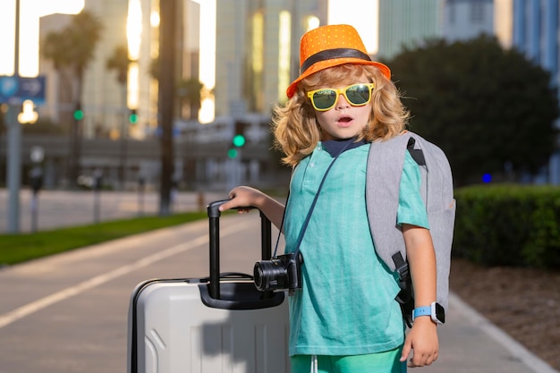 Child traveler standing and holding suitcase outdoor Tourist kid boy having cheerful holiday trip Child travel with travel bag Child with suitcase dreams of travel adventure vacation