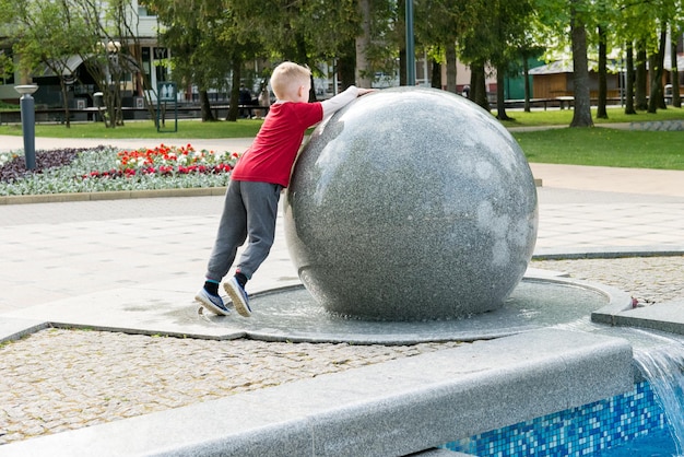 Ребёнок поворачивает большой каменный шар возле фонтана.