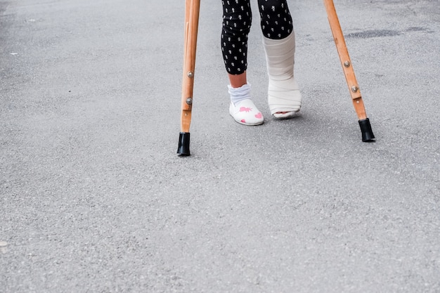 Photo child using crutches and broken legs for walking outdoor,close up. broken leg, wooden crutches, ankle injury.