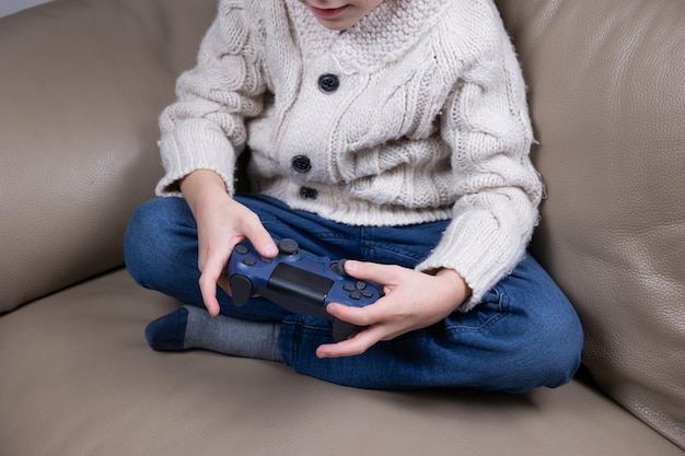 Child using technology The boy sits on the couch holds a game joystick and plays video games