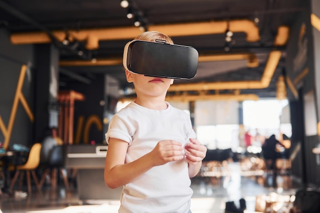 Child in virtual reality eyewear and in casual clothes have fun in playroom