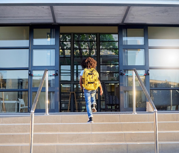 Foto bambino che cammina e ingresso a scuola per l'apprendimento dell'istruzione o lo sviluppo dell'infanzia presso l'edificio dell'accademia bambino che fa una passeggiata su per i gradini pronto per tornare a scuola la mattina con lo zaino per la conoscenza