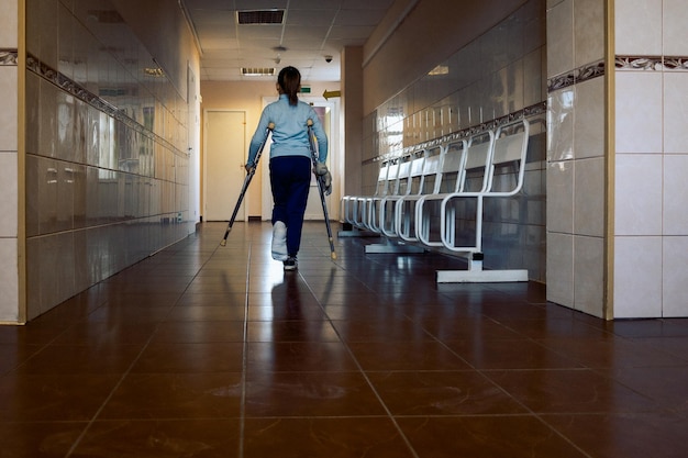 Child walks along hospital corridor on crutches to see doctor girl has one leg broken in cast