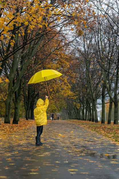 Child walks in rain in park with an umbrella in hands Vertical frame