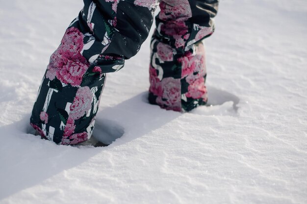 子供は花の散歩のイメージで暖かいズボンで子供の足の雪の吹きだまりのクローズアップビューを歩きます...