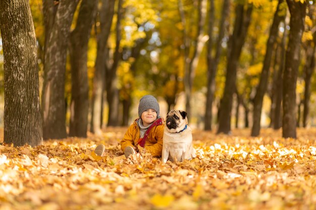 A child walks with a pug in the autumn park. Friends since childhood