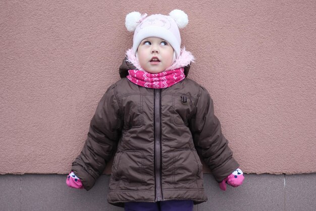 Child in warm cloth in winter season looking up and aside on the purple background