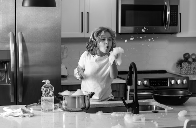 Child washing dishes near sink in kitchen child with sponge with dish washing liquid is doing the