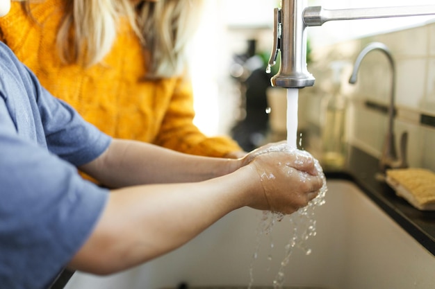 child washing hands under faucet water flowing hygiene focus woman watching the boy washing hands at sink for hygiene and cleanliness boy washing his hands with the help of his mother at home