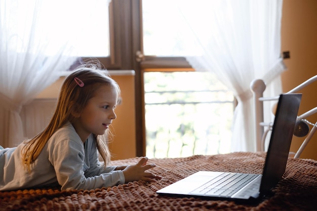 写真 子供がラップトップでアニメを見てベッドで家でテクノロジーを使っている深刻な子供がオンラインで時間を費やしています