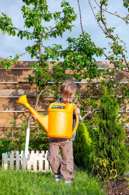 Child watering can watering a garden in the backyard