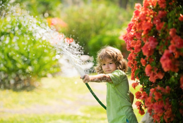 Child watering flowers and plants in garden kid with water hose in backyard kids gardening kids summ