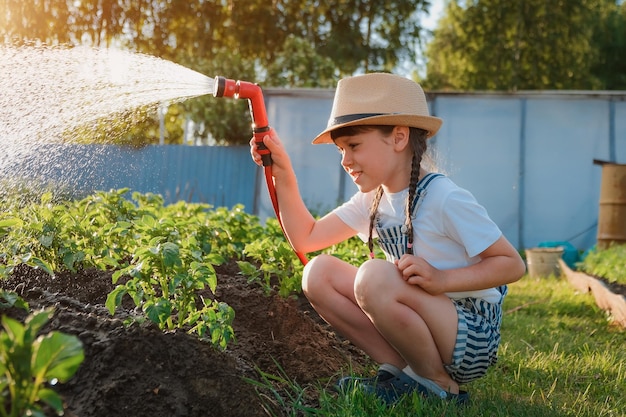 Piante di irrigazione per bambini in giardino bambino con tubo dell'acqua nel cortile soleggiato bambina giardinaggio estate o