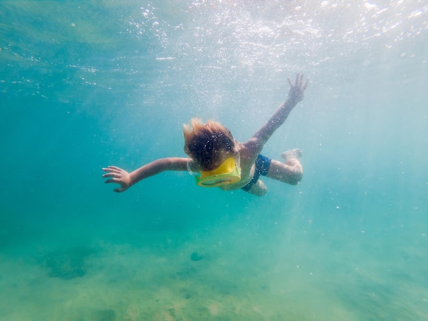 Child wearing snorkeling mask diving underwater in the sea