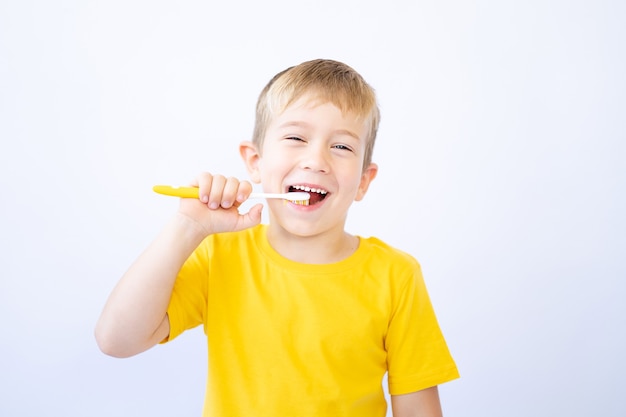 a child on a white background is brushing his teeth holding a toothbrush in his hands isolate