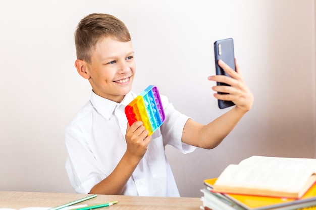 A child in a white shirt sits at a table and takes a selfie with an antistress toy