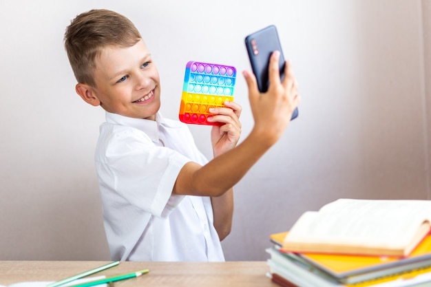 A child in a white shirt sits at a table and takes a selfie with an antistress toy