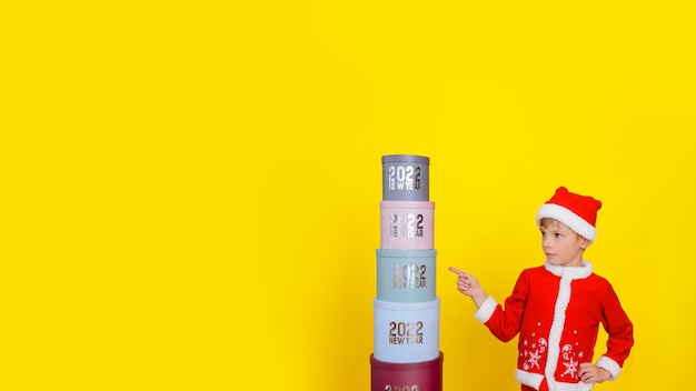 Child who stands near a tower of gift boxes with the text new year 2022 points his finger at boxes