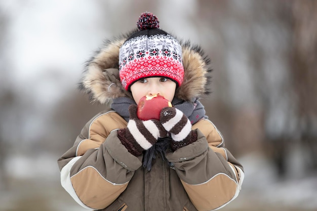 Ребенок зимой с фруктами Мальчик ест красное яблоко