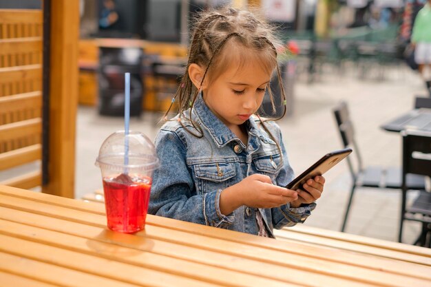 Un bambino con afropigtails in una giacca di jeans sta giocando su uno smartphone