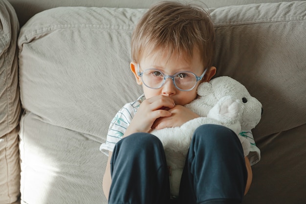Photo a child with autism in glasses sits on the sofa and sad