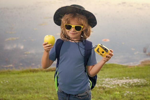 カメラを持った子供が屋外を旅しています夏の日にバックパックを持った少年旅行者野生動物を探検する小さな男の子の肖像画ハイキングとアドベンチャーコンセプト