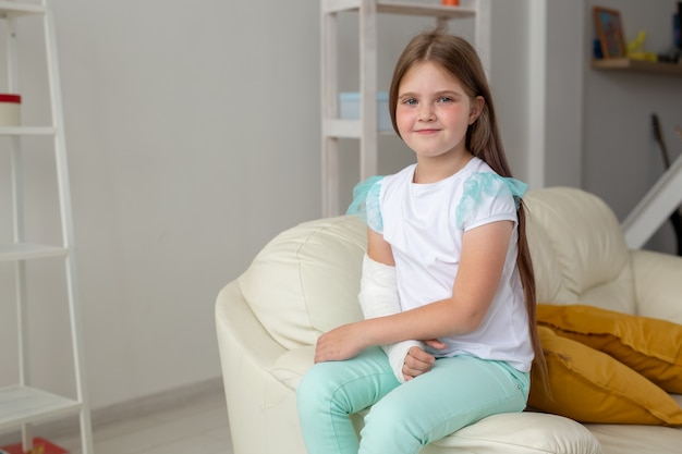 Child with a cast on a broken wrist or arm smiling and having fun on a couch. Positive attitude