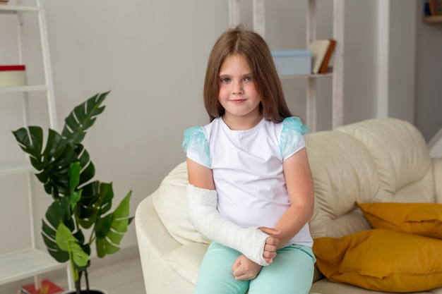 Child with a cast on a broken wrist or arm smiling and having fun on a couch