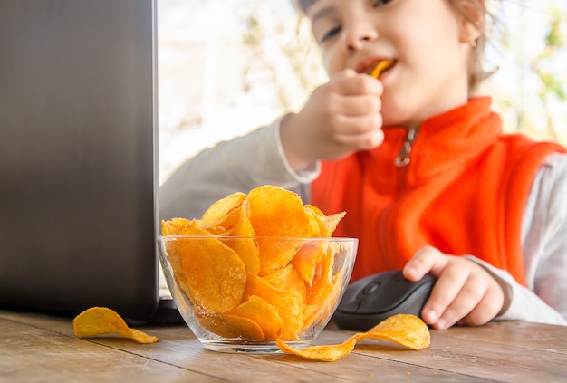 Bambino con patatine fritte dietro un computer