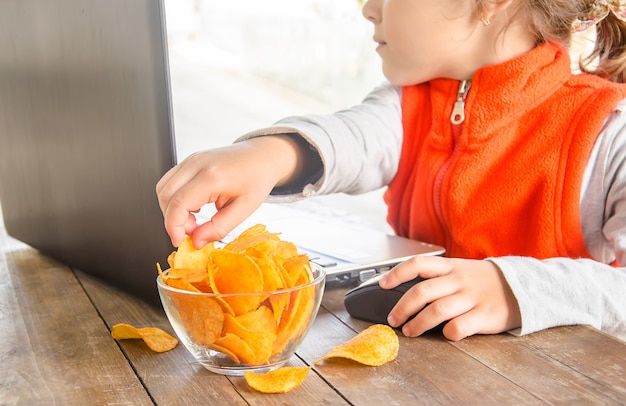 Child with chips behind a computer