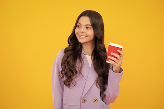 Child with coffee or tea cup isolated on yellow studio background Teenage girl with take away beverage Happy face positive and smiling emotions of teenager girl