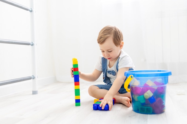 A child with a constructor at home, a cute boy plays or collects a colored constructor