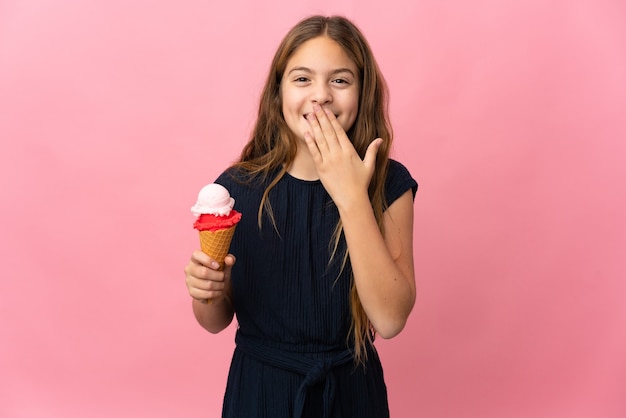 Child with a cornet ice cream over isolated pink background happy and smiling covering mouth with hand